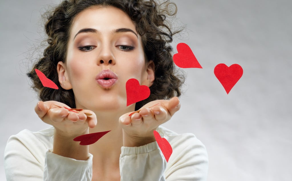 woman blows red paper hearts into camera