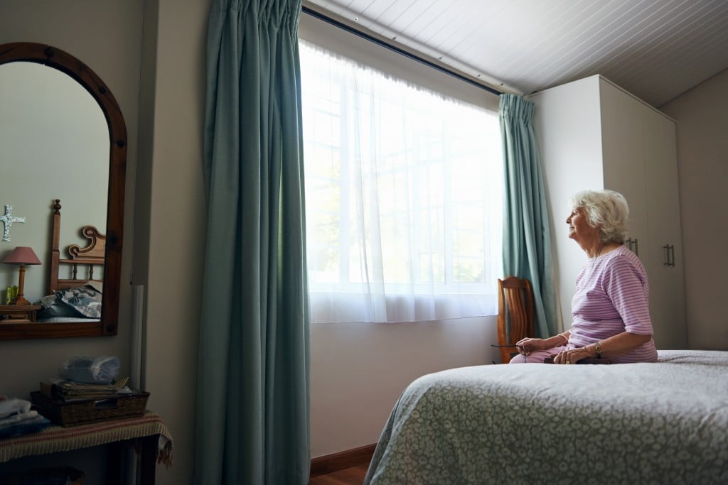 old lady sits on bed and looks out window