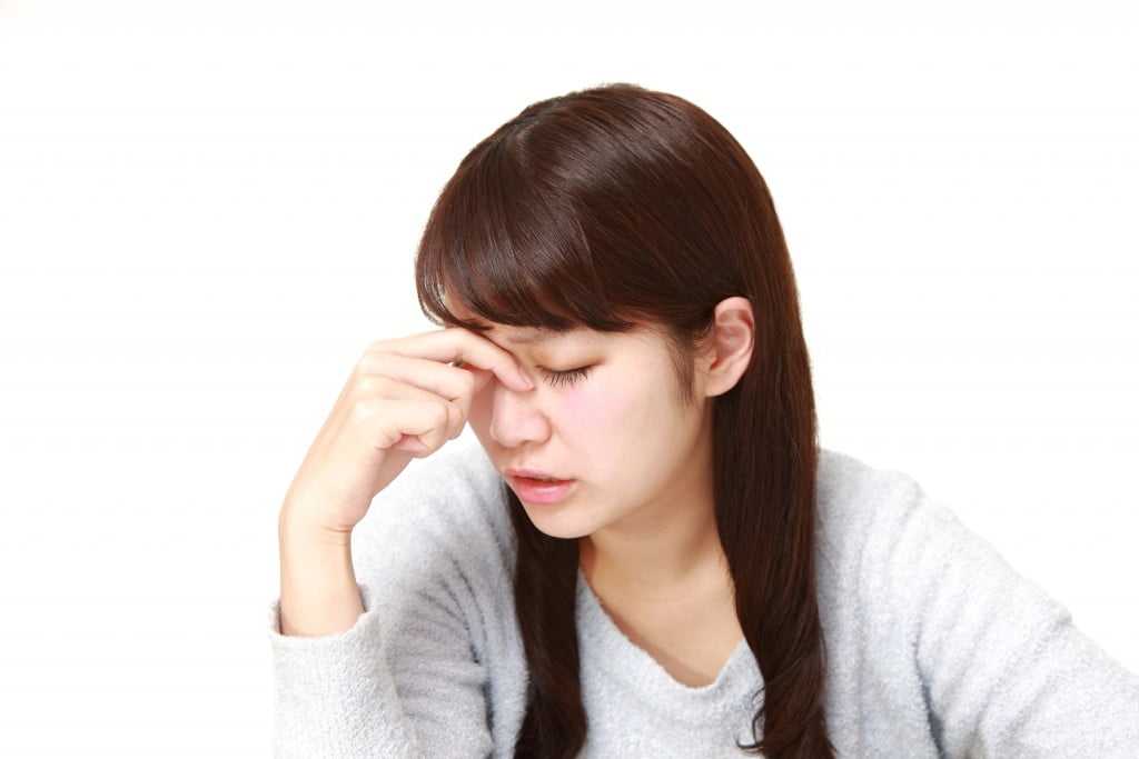 fatigue: young woman looks down and pinches nose between eyes