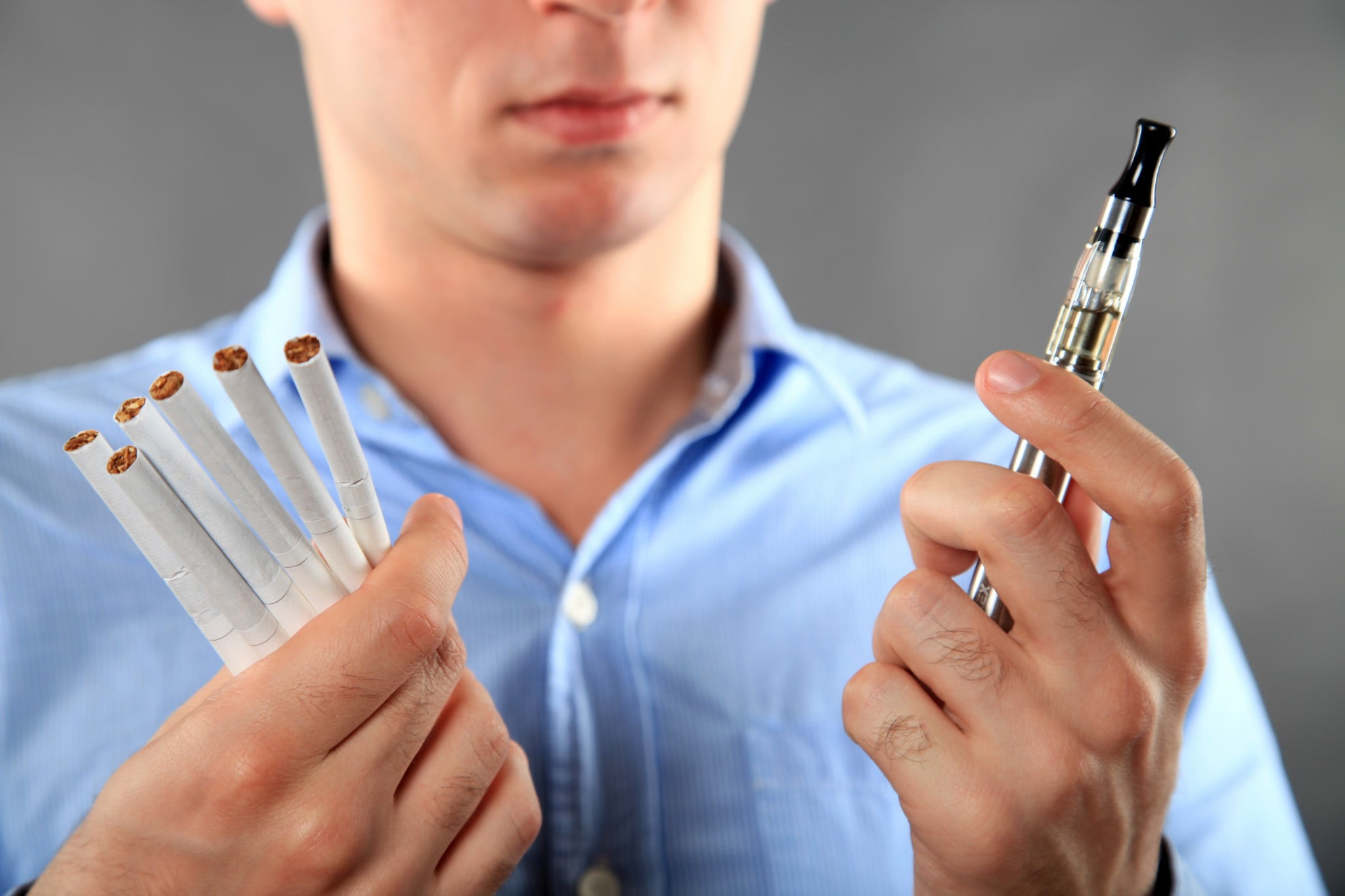 man with e-cigarette in one hand and six cigarettes in the other
