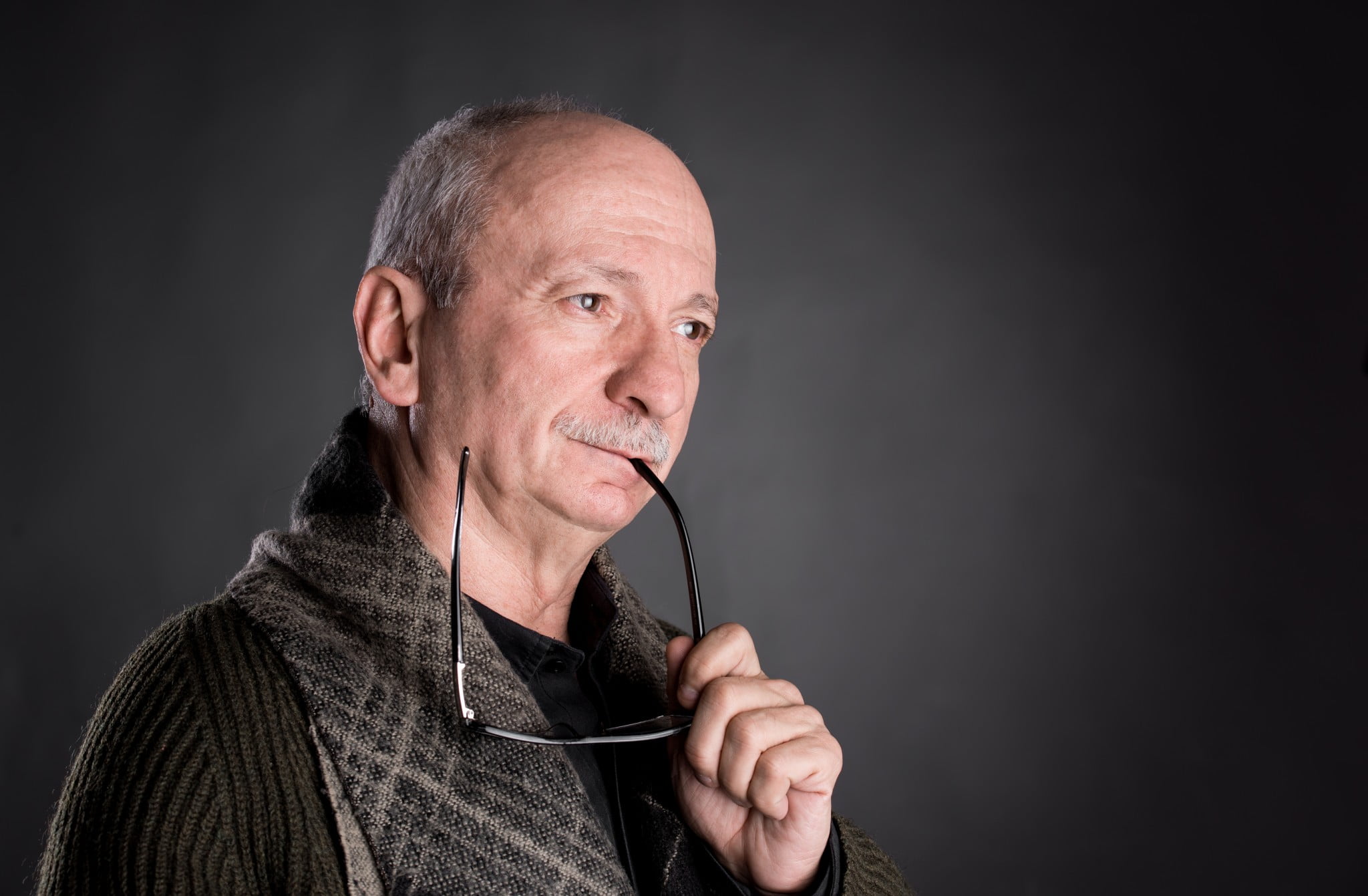 shingles vaccine story: older man looks sad and pensive, chews on end of glasses