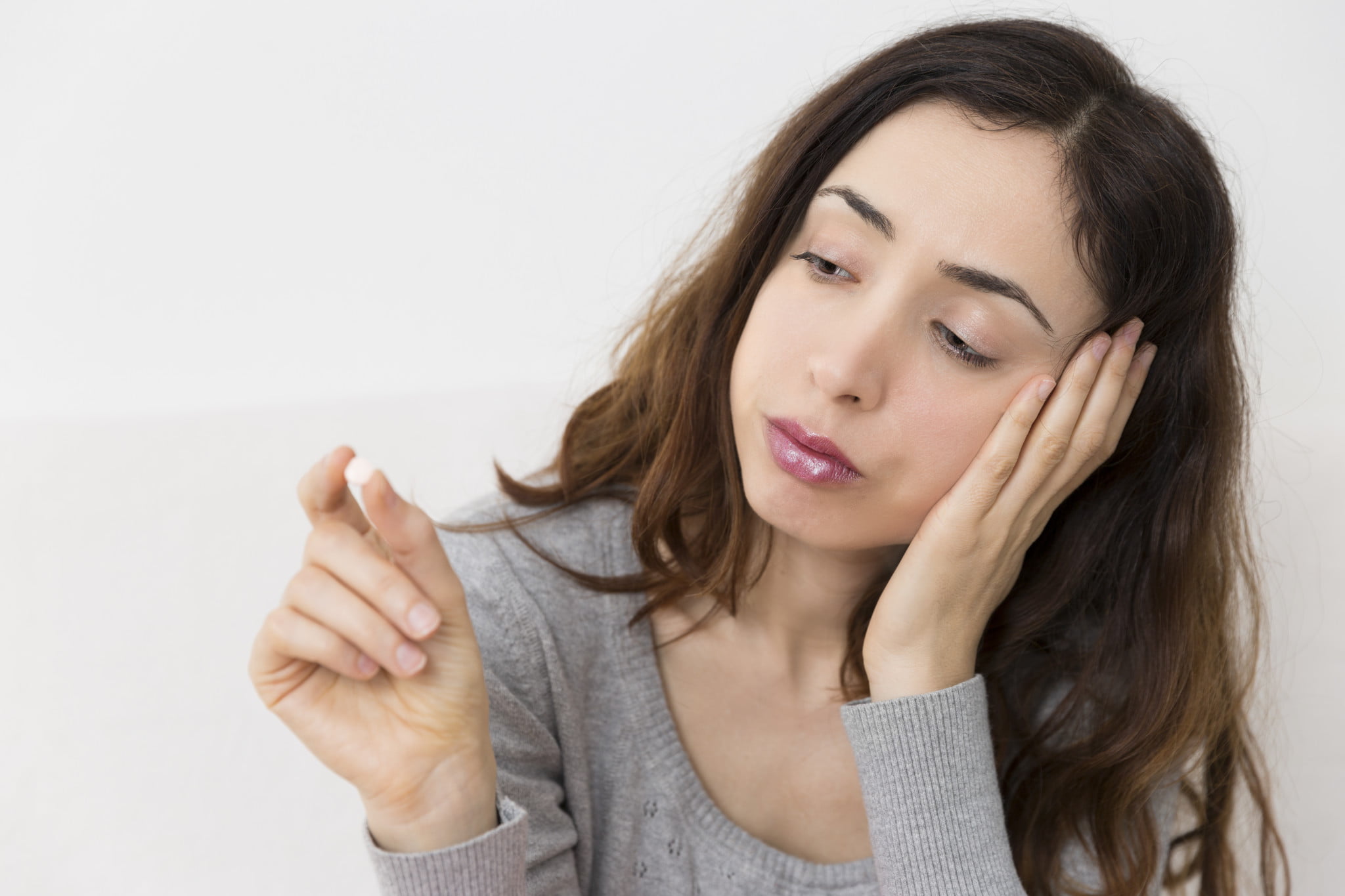 codeine shoppers: sad woman examines a white tablet