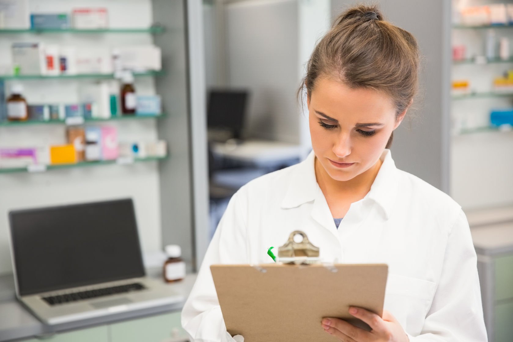 bored-looking young pharmacist writing on a clipboard