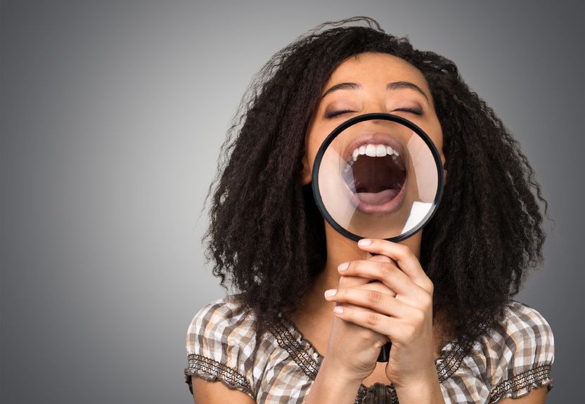 dental and oral problems: woman says "aah" into magnifying glass to show white teeth