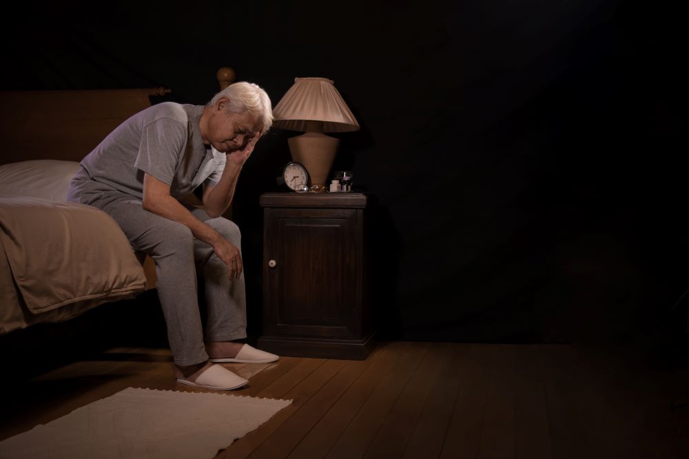 senior man awake sitting on bed looking upset